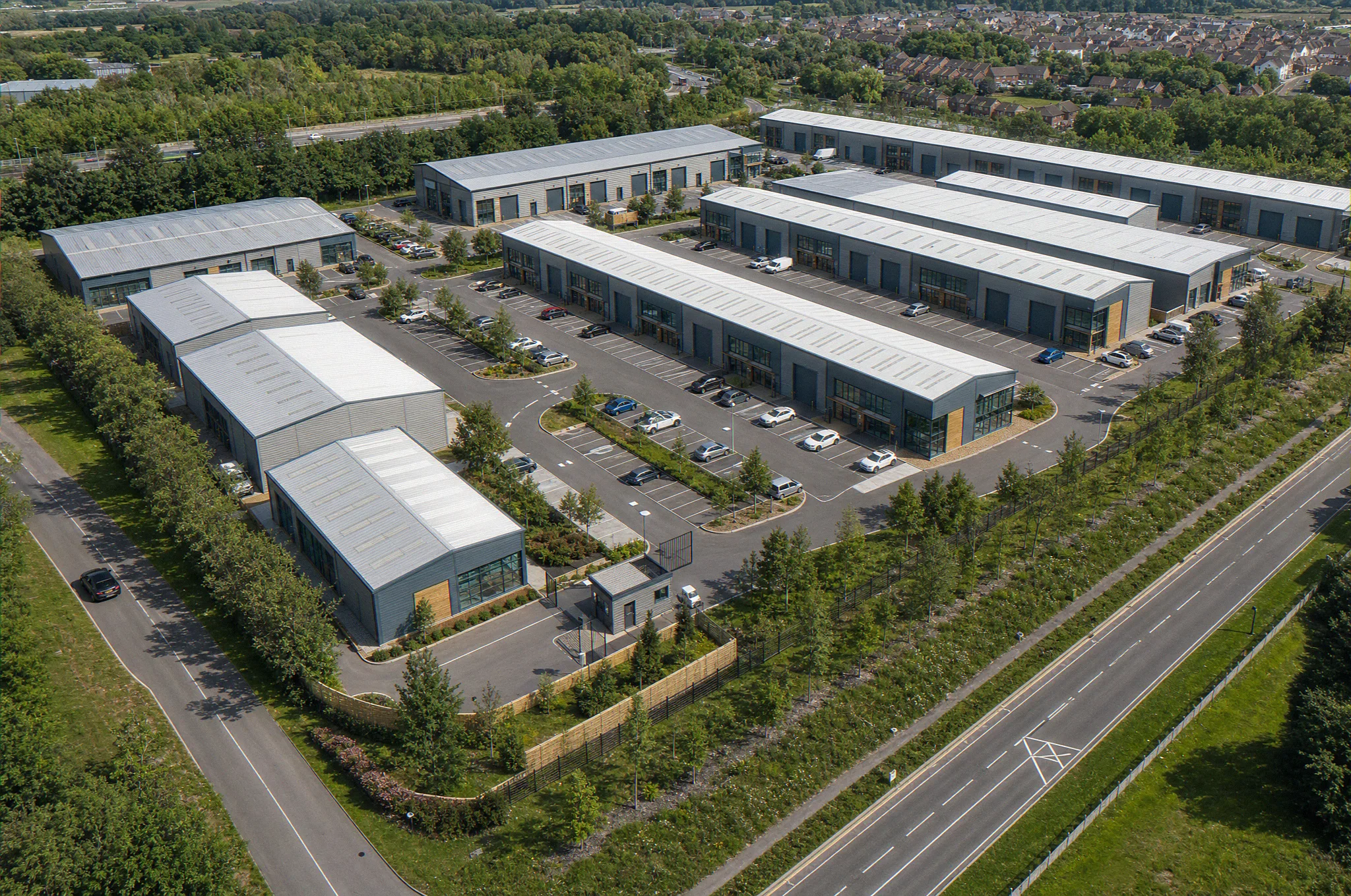Light industrial estate master plan CGI, high oblique aerial view of a multi-let light industrial scheme with terraces of units, internal estate roads, shared parking courts, a gatehouse entrance, and a landscaped boundary, industrial architectural visualisation by StratumCGI