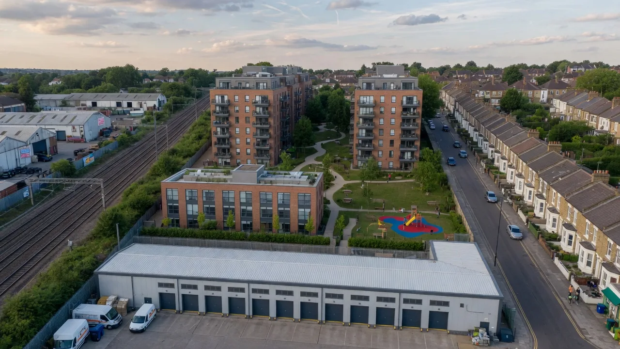 Aerial mixed-use CGI of a co-location masterplan: a light industrial block and yard in front of two residential blocks around a podium courtyard, beside a railway line