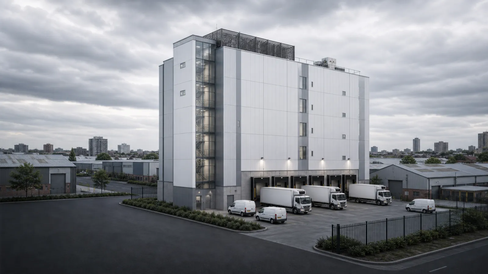 Vertical urban cold storage CGI showing a taller smaller-footprint in-city refrigerated warehouse with ground-level dock doors, compact service yard, light-industrial neighbours, last-mile cold chain logic for urban grocery and dark-store distribution, and insulated metal panel envelope appropriate for urban edge sites, industrial architectural visualisation by StratumCGI