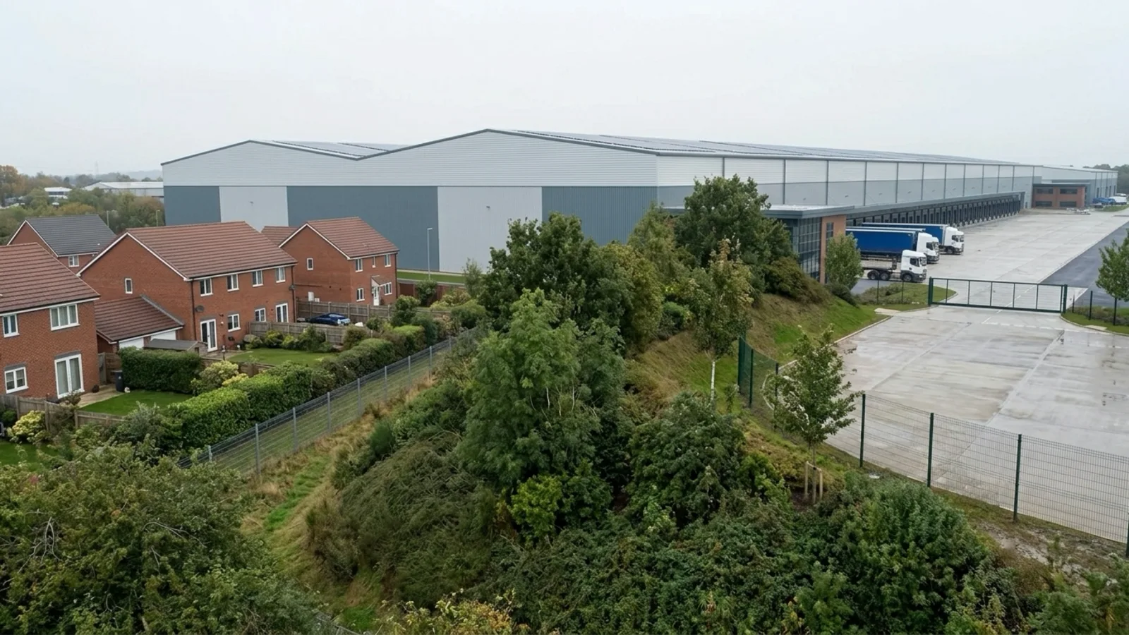 Planning CGI still of a UK warehouse showing massing, landscape screening, and neighbour houses from the site boundary